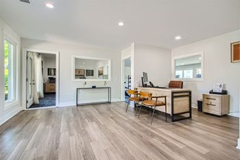 a living room with a desk and chairs and a kitchen